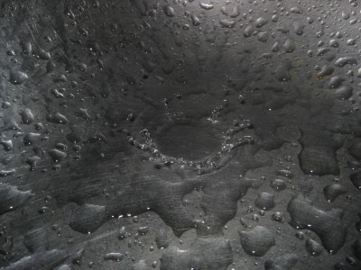 Water drops from the faucet hitting the bottom of the sink.